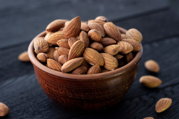 Almonds nuts in ceramic bowl on on the dark oak texture