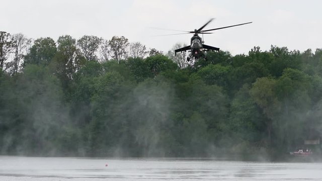Heavy Russian attack helicopter sprays water into the air, water vaporizes from rotor downdraft, front view of Soviet-built Mi-24 Hind flying low level above water.