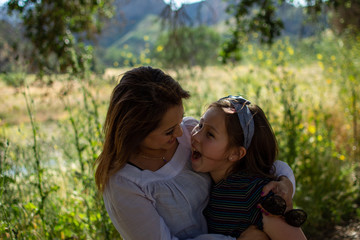 Latina Woman and daughter smiling together in front of a bright field at a park