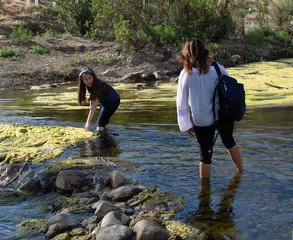 Woman crossing a stream with  daughter playing in a stream or river
