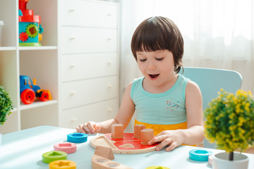 little girl collects a wooden unpainted pyramid. Safe natural wooden children's toys.