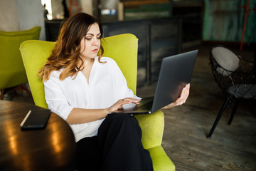 A young, sympathetic woman, not a thin-headed body building, sits in a cozy cafe and works for a laptop. Business clothing style.