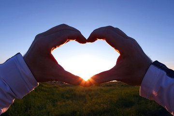 clasped hands in heart shape on a background sunset