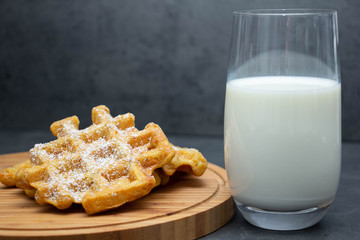 carrot waffles with powdered sugar on a wooden board with a glass of milk. Perfect healthy breakfast.