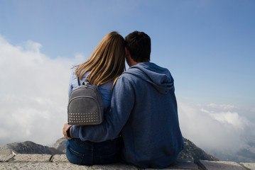 Romantic date in the mountains. A couple in love sits in an embrace and admires the beautiful landscape. Rear view, blonde girl and brunette guy.