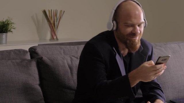 smiling busines man with headphones talking by phone sitting on sofa