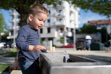 Little boy at the public fountain playing with water drinking in summer sunny day thirsty refreshment