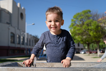 Little boy at the public fountain playing with water drinking in summer sunny day