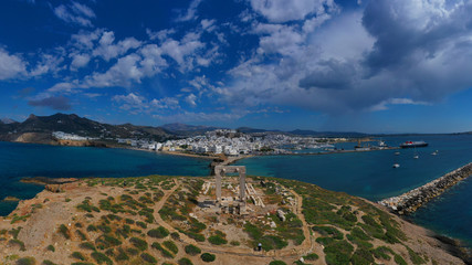 Aerial drone panoramic view of iconic and unique Temple of Apollon or Portara (Gate) with breathtaking views to port - town and castle of Naxos island and the Aegean blue sea, Cyclades, Greece