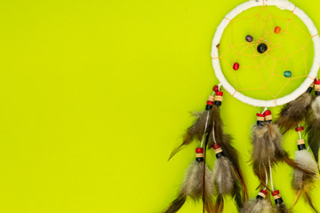 Dreamcatcher with brown bird feathers, and with threads and beads of rope hanging. Dreamcatcher handmade. Lies on a green background.