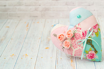 One textile heart with a romantic flower color on a simple light wooden background. selective focus. Shabby chic style.