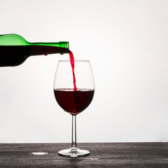 Red wine is poured from a glass green bottle into a glass on a white background.