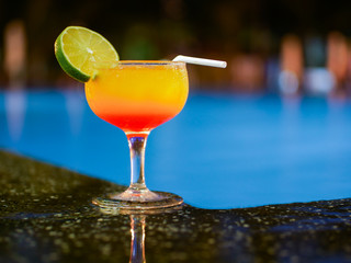 yellow-red cocktail stands on the edge of the pool