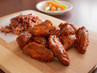 Fried Chicken Wings Covered in True Hot BBQ Sauce with a side of Cole Slaw Carrots and Celery served on a Cutting Board