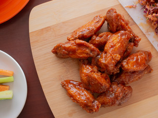 Fried Chicken Wings Covered in True Hot BBQ Sauce with a side of Cole Slaw Carrots and Celery served on a Cutting Board