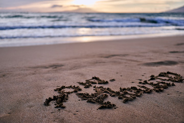 A couple's initials and a heart shape scribbled on the sands of a beach at Maui, Hawaii during sunset.