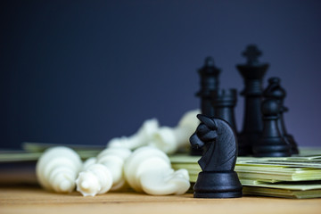 Black chess stands on top of dollar banknotes and wooden tables with white chess is falling. Concept of win or advantage and defeat of business competitors