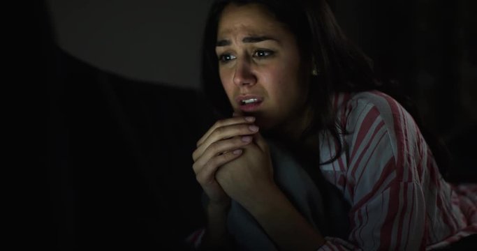4K Close up face of young woman watching a scary movie on computer late at night. Slow motion.