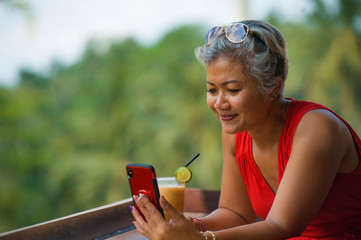 attractive and relaxed Asian woman with grey hair and stylish red dress using social media on...