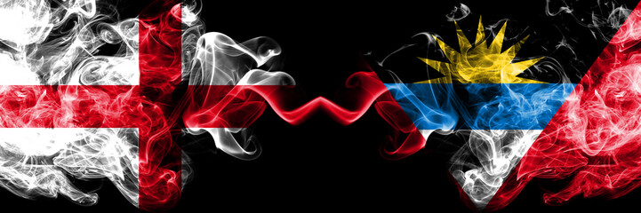 English vs Antigua and Barbuda smoky mystic flags placed side by side. Thick colored silky smokes flag of England and Antigua and Barbuda.