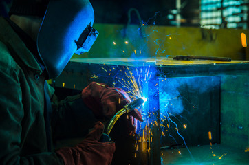 The worker in overalls and a protective mask welds metal with a welding machine. Profession welder....