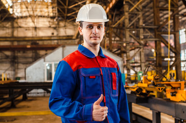 A man is showing his thumb up. An employee in overalls and a white helmet of an industrial plant shows a class. Gestures.