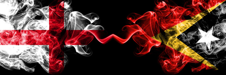 English vs East Timor smoky mystic flags placed side by side. Thick colored silky smokes flag of England and East Timor.