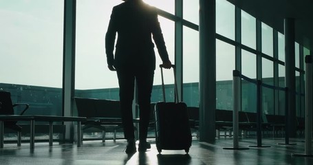 Slow motion of an young elegant businessman in a suit is walking with a suitcase in the international airport with a sunshine from the window. - Powered by Adobe