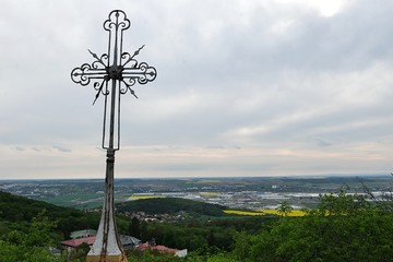 Steel decorative christian cross above cave of Saint Svorad near bottom of Zobor hill, Nitra, Slovakia. Roofs of pulmonary disease hospital are visible under the cross, Nitra center in background  