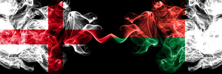 English vs Madagascar, Madagascan smoky mystic flags placed side by side. Thick colored silky smokes flag of England and Madagascar, Madagascan.