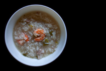 Rice congee mixed with shrimp and pork in white bowl on black background.