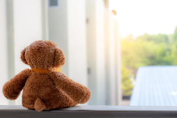 Brown teddy bear sitting vacant alone at the terrace with nature blurred background, Absent-minded and waiting for someone concept.