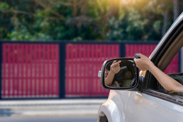 Young woman in car, hand using remote control to open the automatic gate while phoning and leaving...