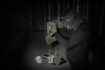 Robber in a mask and with a flashlight examines the contents of the women's bag in a dark room