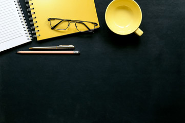 Dark leather office desk with cup of coffee, pen,glasses and yellow notebook. Top view.