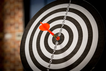 Red dart arrow hitting in the target center of dartboard on bullseye with sun light vintage style,...