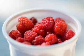 Lots of ripe red raspberries in a white plastic Cup. Horizontal photography