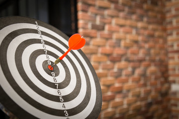 Red dart arrow hitting in the target center of dartboard on bullseye with sun light vintage style,...