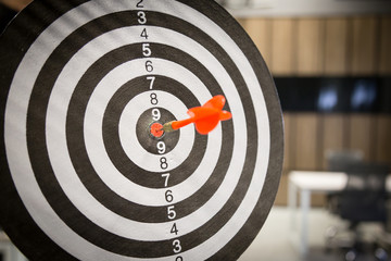 Red dart arrow hitting in the target center of dartboard on bullseye with sun light vintage style,...