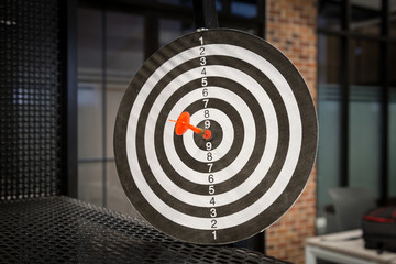 Red dart arrow hitting in the target center of dartboard on bullseye with sun light vintage style,...