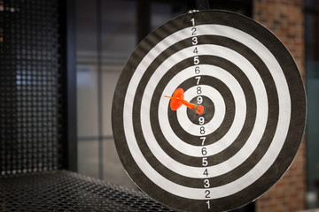 Red dart arrow hitting in the target center of dartboard on bullseye with sun light vintage style,...