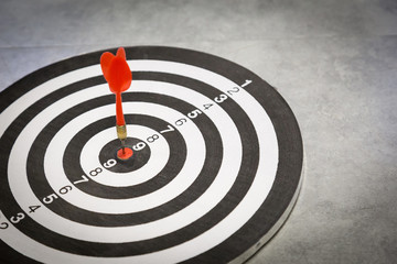 Red dart arrow hitting in the target center of dartboard on bullseye with sun light vintage style,...