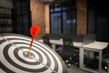 Red dart arrow hitting in the target center of dartboard on bullseye with sun light vintage style,...