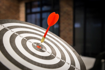 Red dart arrow hitting in the target center of dartboard on bullseye with sun light vintage style,...