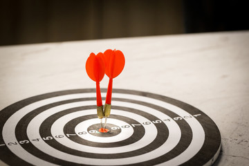Red dart arrow hitting in the target center of dartboard on bullseye with sun light vintage style,...