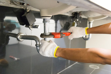 Plumber fixing white sink pipe with adjustable wrench.