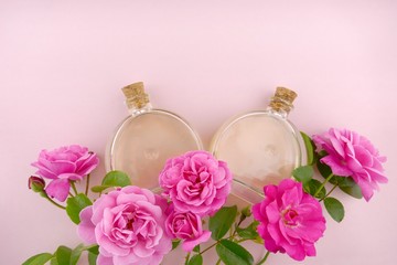 Rose essential oil in a round glass bottles set and double roses flowers on a gently pink pastel background.Natural organic nature oils. Aromatherapy.copy space	