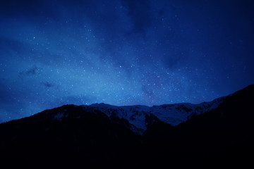 Fototapeta na wymiar mountain ridge covered with snow-capped peaks winter night with stars and milky way galaxy