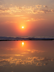Obraz premium sunrise with waves and reflection on still water with clouds