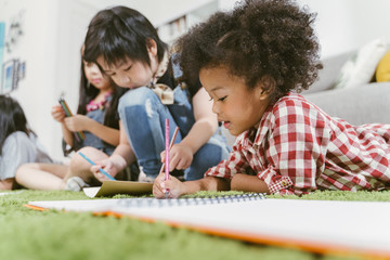 Group of little preschool kids drawing paper with color pencils . portrait of African girl with...